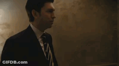Man In Suit Standing By Blackboard In Dark Room GIF