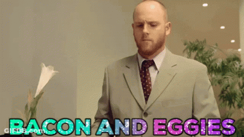 Man In Suit Standing In Front Of Sign Saying Bacon And Eggies GIF