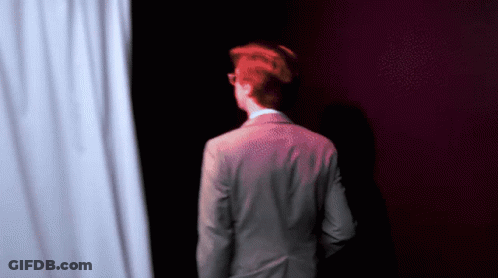 Man In Suit Standing In Front Of White Curtain GIF