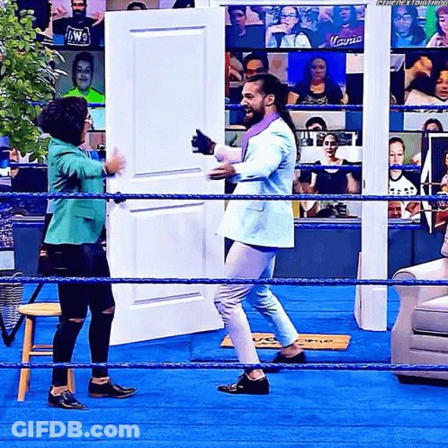 Man In Suit Standing In Wrestling Ring With Woman In Green Jacket GIF
