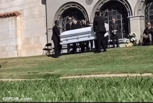 Man In Suit Standing Next To Coffin GIF