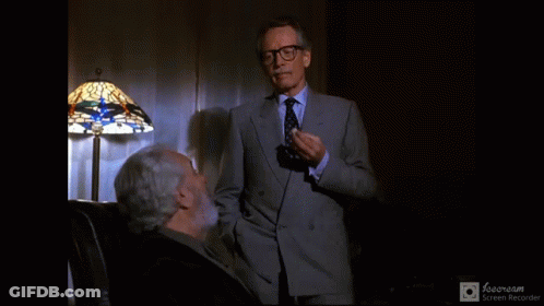 Man In Suit Standing Next To Man In Chair GIF