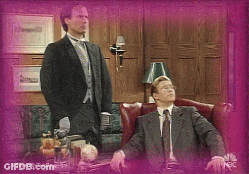 Man In Suit Standing Next To Seated Man GIF
