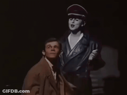 Man In Suit Standing Next To Woman In Hat GIF