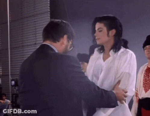 Man In Suit Standing Next To Woman In White Shirt GIF
