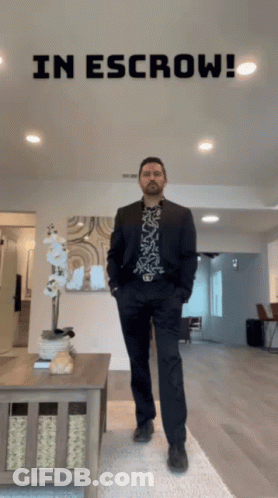 Man In Suit Stands In Living Room With In Escrow Behind GIF