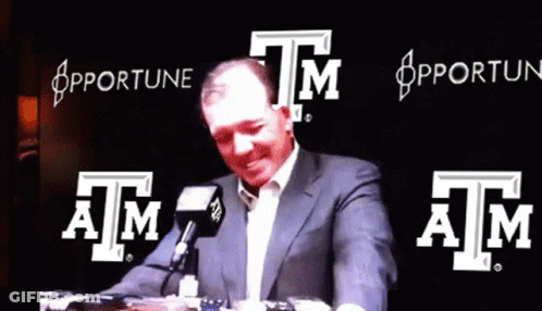 Man In Suit Talking Into Microphone In Front Of Apfortune Sign GIF