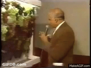 Man In Suit Talking Into Microphone In Front Of Refrigerator Filled With Vegetables GIF