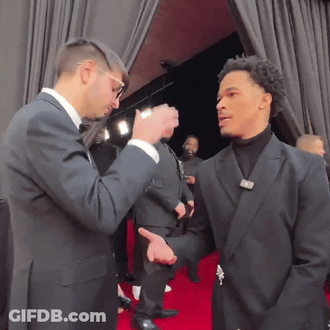 Man In Suit Talking To Another In Black Suit On Red Carpet GIF