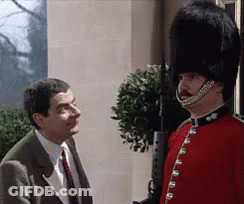 Man In Suit Talking To Man In Red Uniform And Black Hat GIF