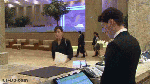Man In Suit Talking To Woman At Counter In Lobby GIF