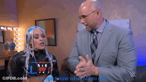 Man In Suit Talking To Woman In Wig Saying Let Me Know What Mami Says GIF