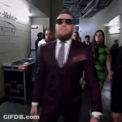 Man In Suit Walking Down Hallway With Group GIF