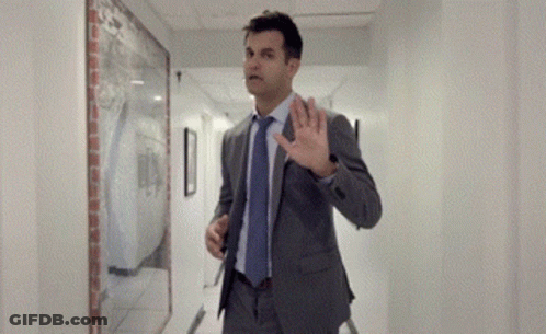 Man In Suit Walking Down Hallway With Hand Up GIF