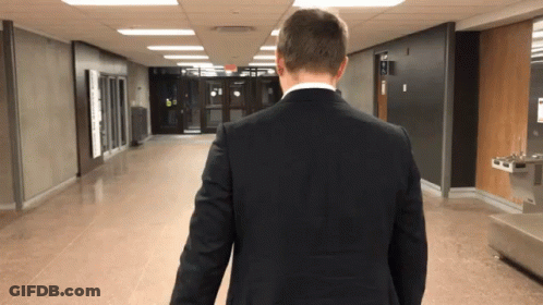 Man In Suit Walking Down Hallway With Water Fountain GIF