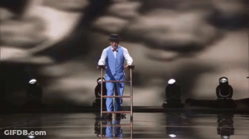 Man In Suit Walking On Stage With Cane And Ladder GIF