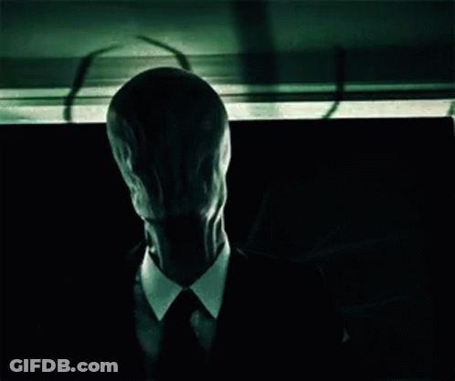 Man In Suit With Long Face Sitting In Dark Room GIF