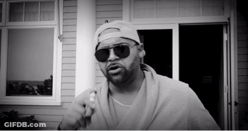 Man In Sunglasses And Baseball Cap Standing In Front Of House GIF