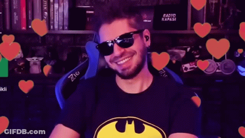 Man In Sunglasses And Batman Shirt Smiling In Front Of Hearts GIF