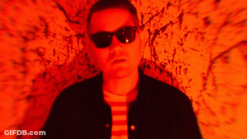 Man In Sunglasses And Black Jacket In Front Of Red Wall GIF