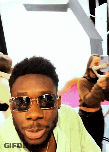 Man In Sunglasses And Green Shirt Looking At Camera GIF