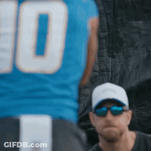 Man In Sunglasses And Hat Beside Football Player In Blue Jersey GIF
