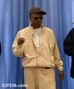 Man In Sunglasses And Hat Dancing In Front Of Blue Curtain GIF