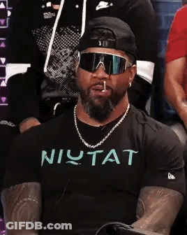 Man In Sunglasses And Hat Smoking Cigarette In Crowd GIF