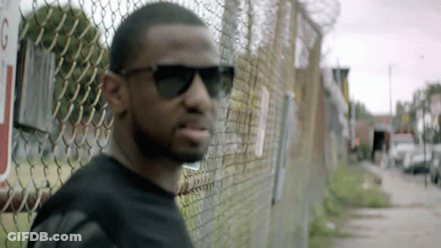 Man In Sunglasses Leaning Against Chain Link Fence GIF