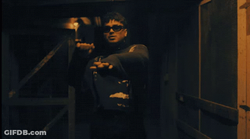 Man In Sunglasses Standing With Hands Outstretched In Dark Room GIF