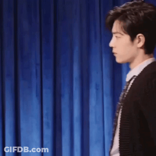 Man In Sweater And Tie Making Fist In Front Of Blue Curtain GIF