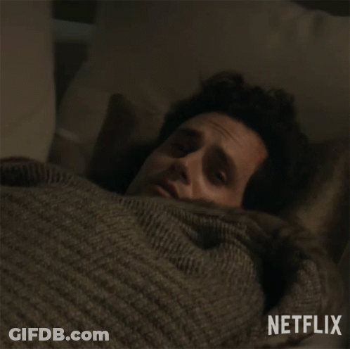 Man In Sweater Laying In Bed With Netflix Logo GIF