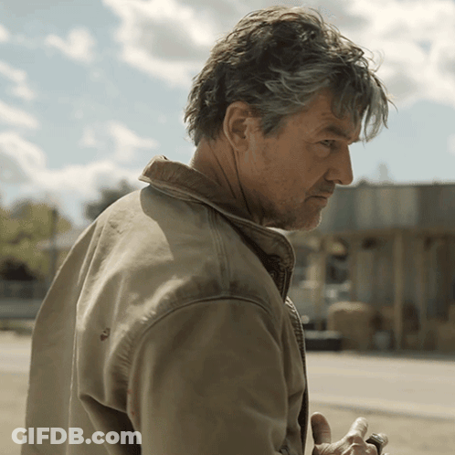 Man In Tan Jacket Standing In Front Of Building GIF