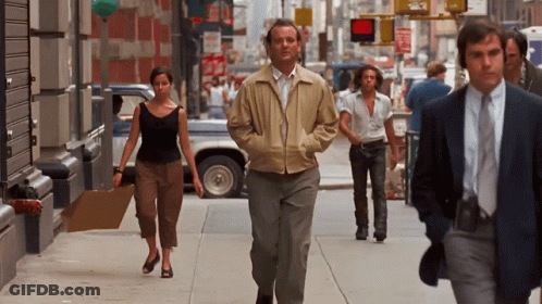 Man In Tan Jacket Walking Down Sidewalk GIF