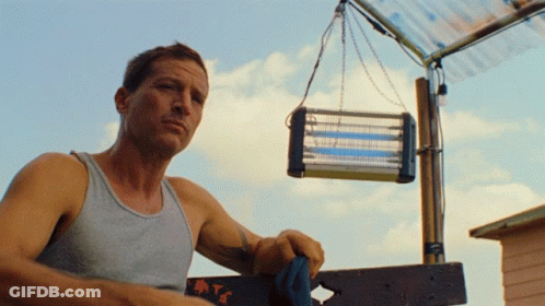 Man In Tank Top Standing Next To Mosquito Killer GIF