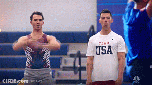 Man In Team USA Shirt Standing Next To Man In Leotard GIF