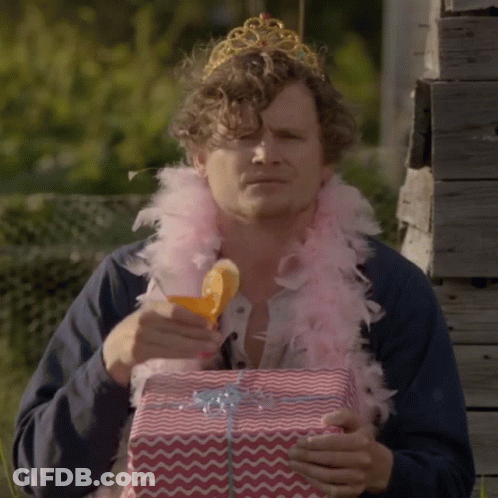 Man In Tiara And Feather Boa Holding Gift Box GIF