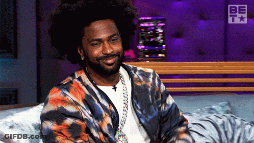Man In Tie Dye Jacket Smiling On Bed GIF