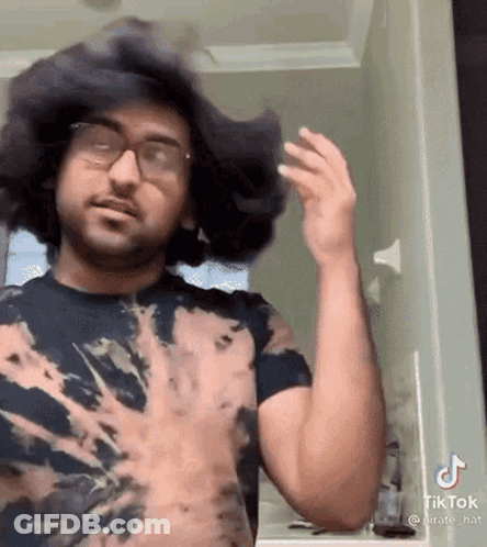 Man In Tie Dye Shirt Standing In Front Of Mirror GIF