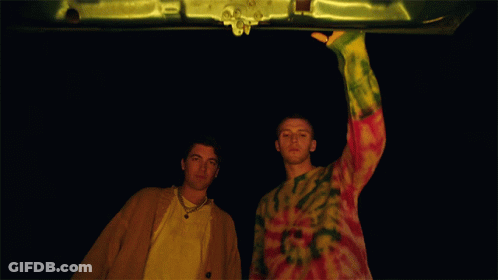 Man In Tie Dye Sweater Next To Man In Yellow Jacket GIF