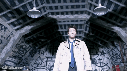 Man In Trench Coat And Tie In Dark Room With Graffiti GIF