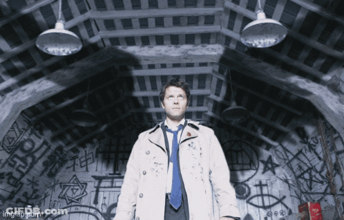 Man In Trench Coat And Tie Standing In Dark Room GIF