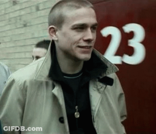 Man In Trench Coat In Front Of Red Wall Number 23 GIF