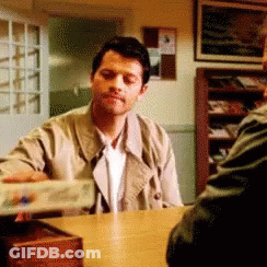 Man In Trench Coat Sitting At Table With Another Man GIF