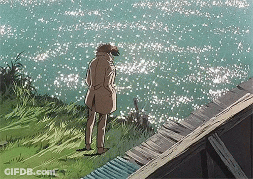 Man In Trench Coat Standing On Cliff Overlooking Ocean GIF