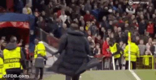 Man In Trench Coat Walking On Soccer Field Surrounded By Security Guards GIF
