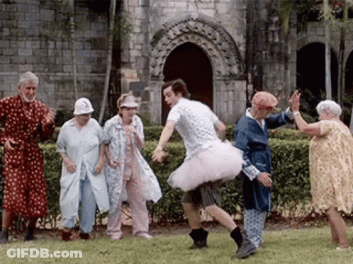 Man In Tutu Dancing With Elderly People In Front Of Building GIF