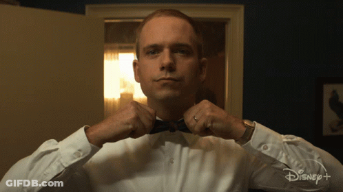 Man In Tuxedo Adjusting Bow Tie In Front Of Disney Plus Sign GIF