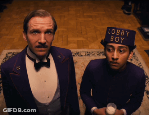 Man In Tuxedo And Man In Lobby Boy Hat GIF