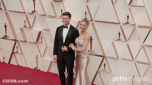 Man In Tuxedo And Woman In Dress On Red Carpet With Oscar Statues GIF